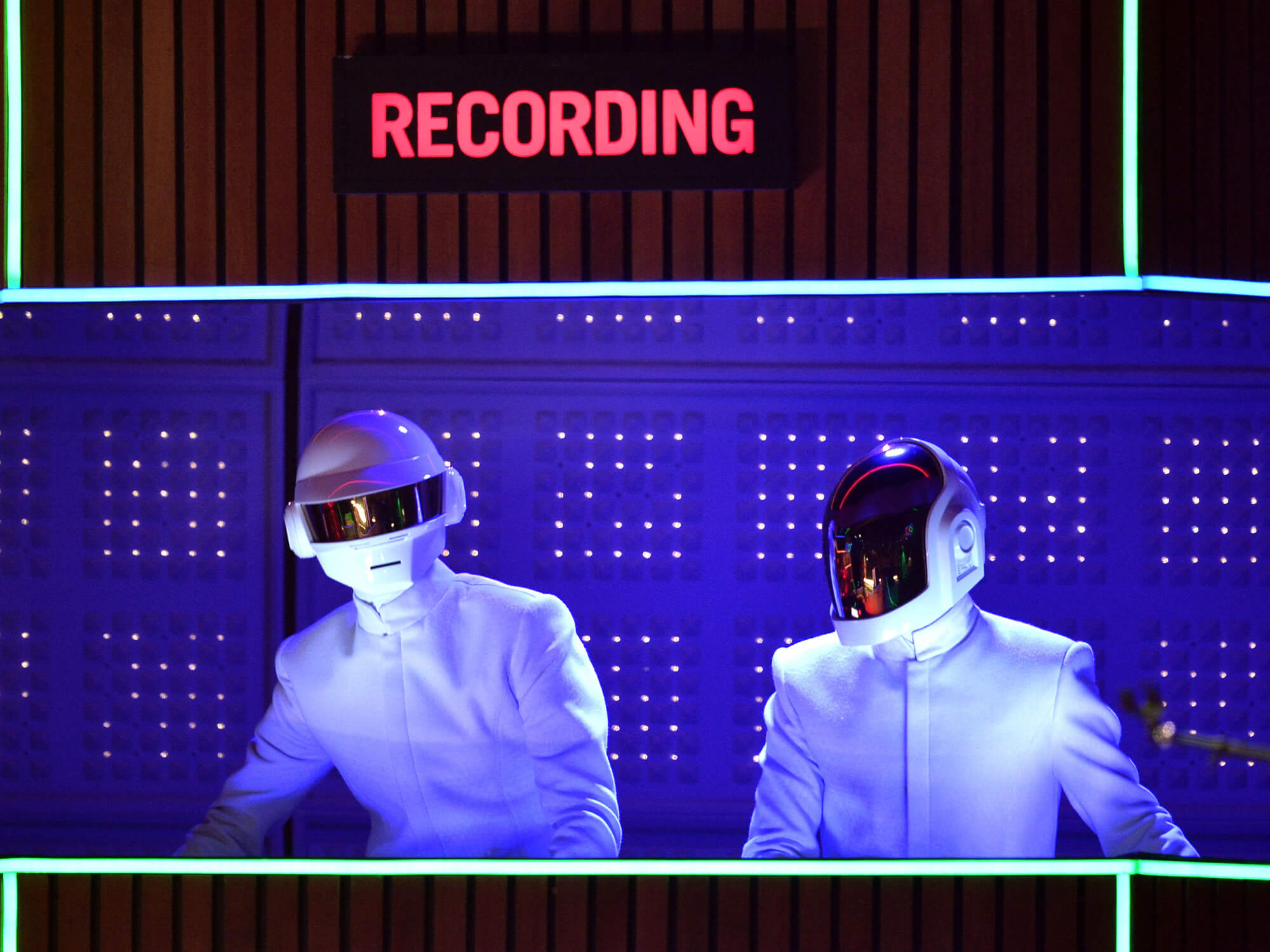 Daft Punk on stage, the word "recording" is illuminated in red above them. They are wearing all white suits and have their famous helmets on