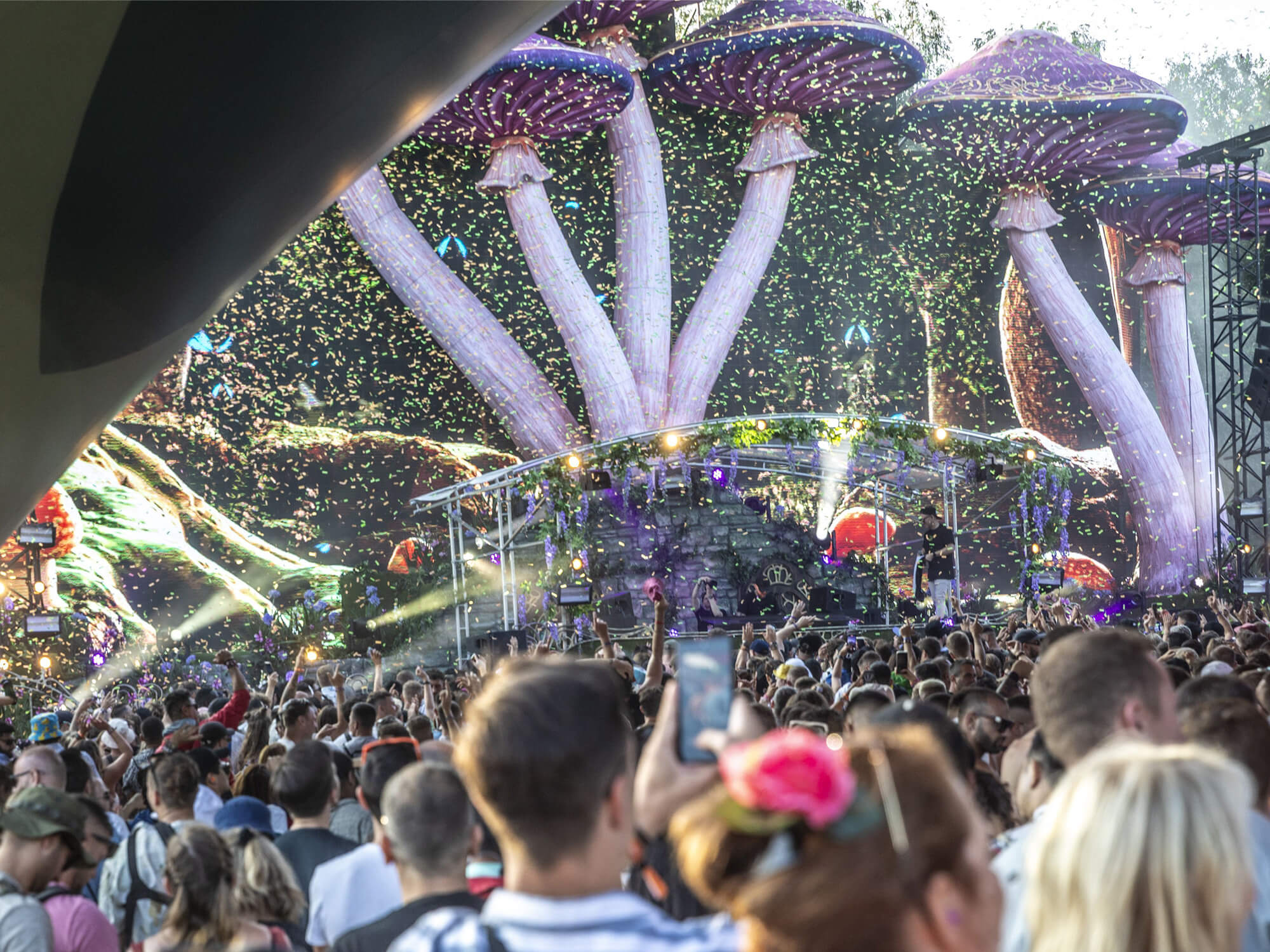 A crowd at Tomorrowland festival. A giant sculpture of mushrooms surrounds a stage.