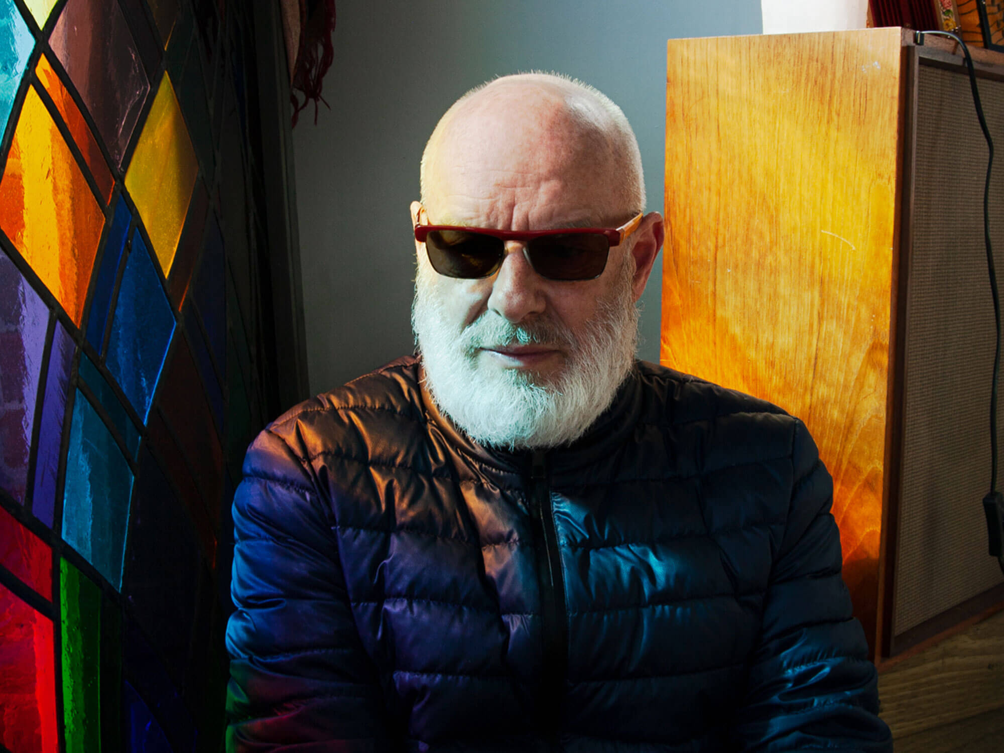 Brian Eno in sunglasses next to a stain-glass window