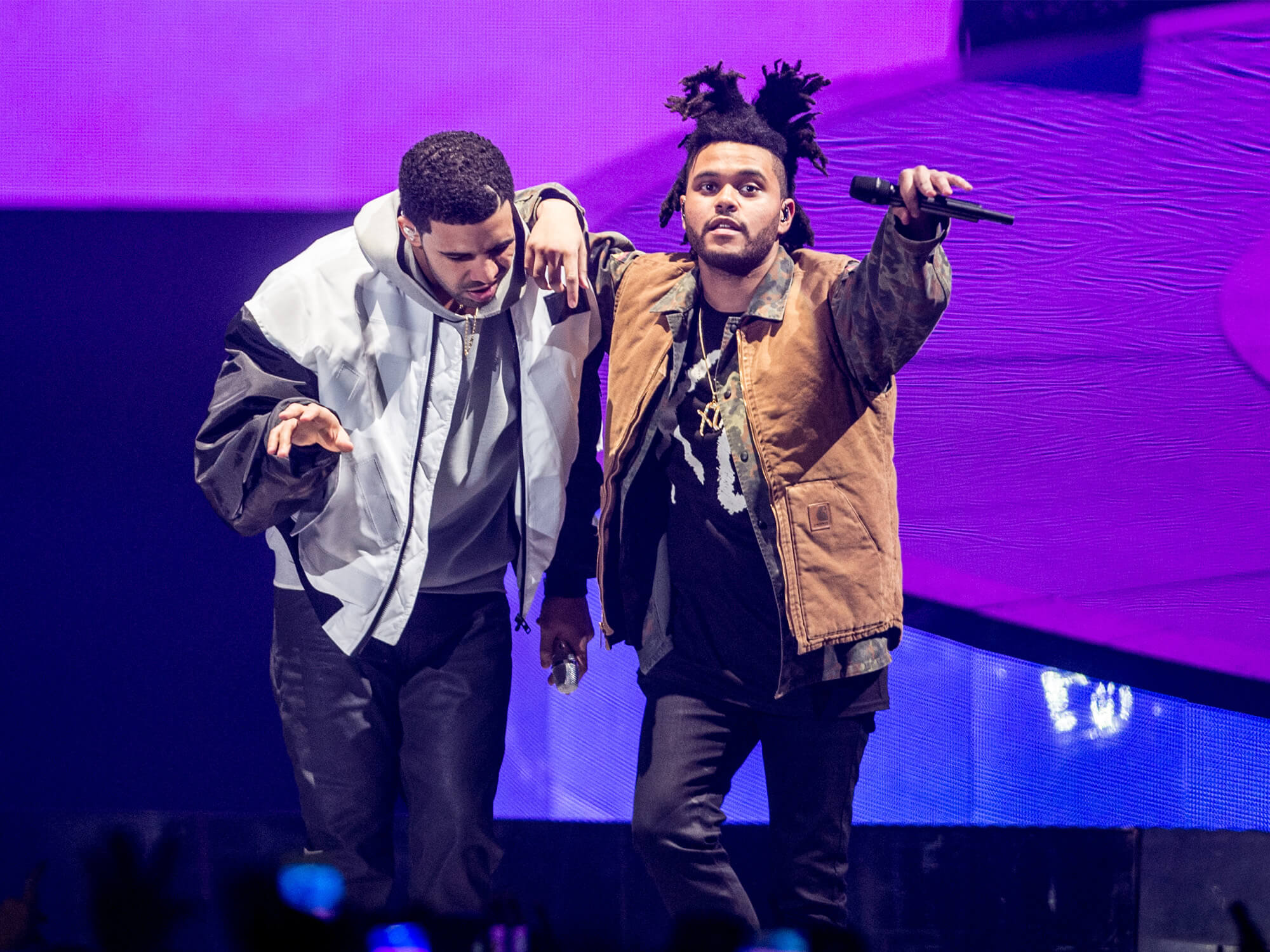 Drake and The Weeknd on stage in 2014. They have their arms around each other and mics in hand.