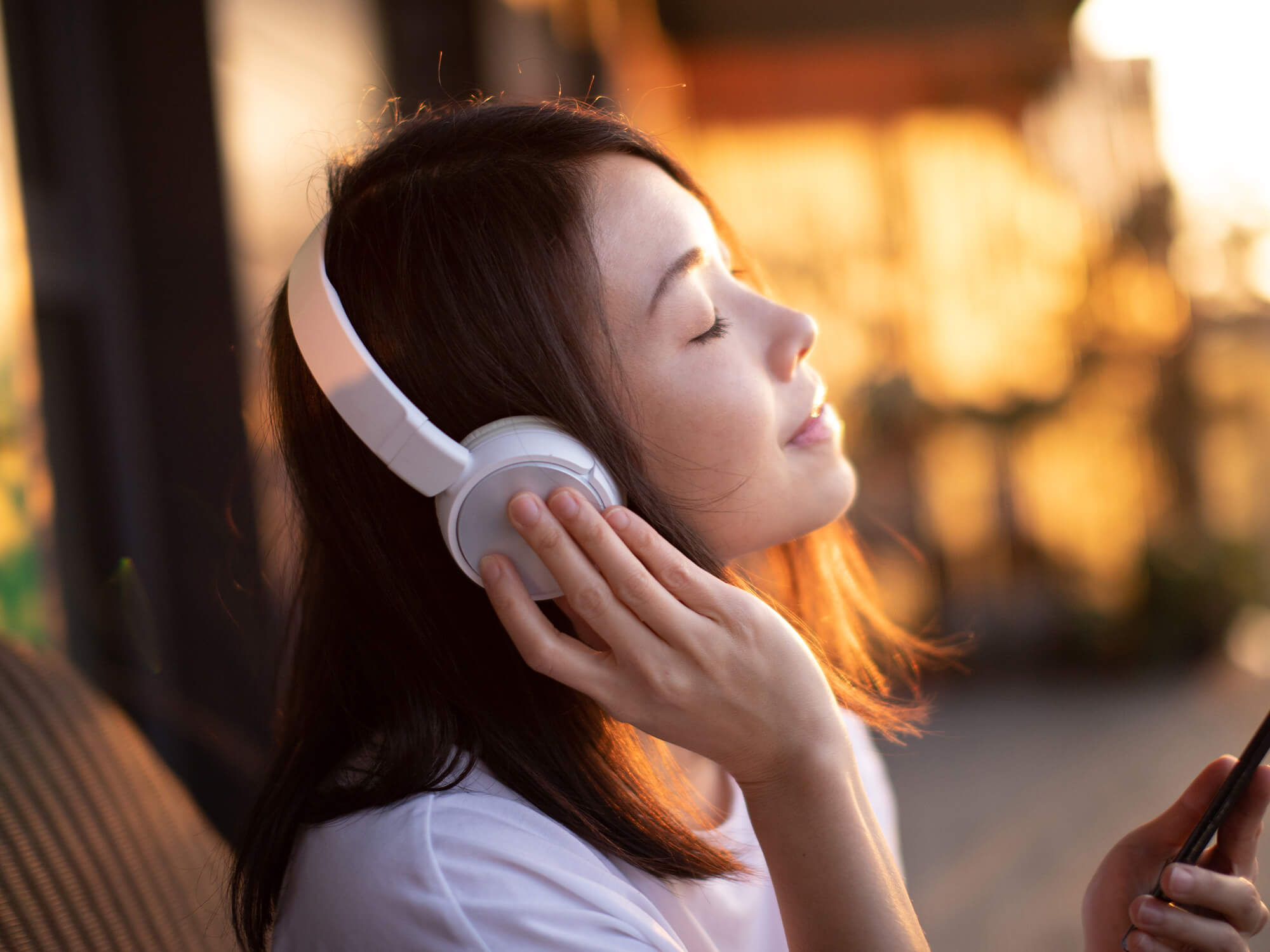 A woman wearing headphones and listening to music. She has her eyes closed and is slightly smiling as if relaxed.