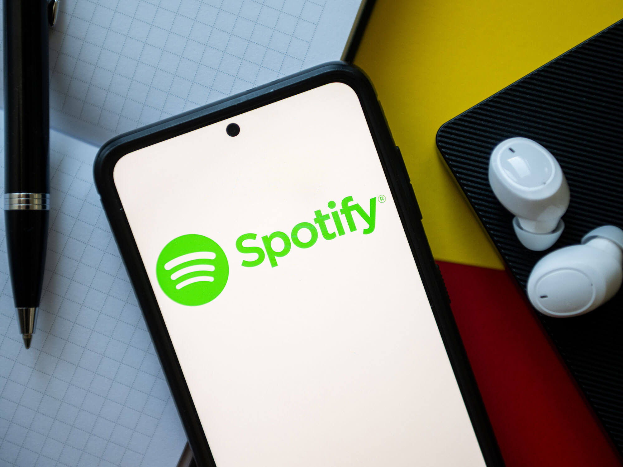 Spotify logo on a phone, sitting on a desk with headphones and a pen