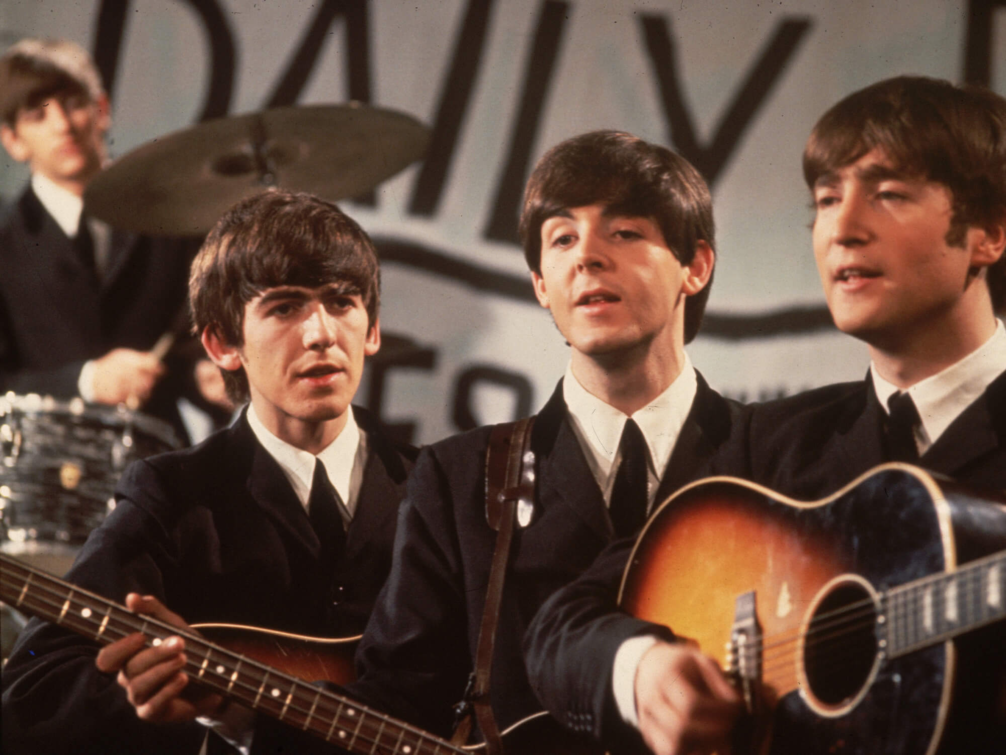 The Beatles. Ringo Starr can be seen behind the drums in the background, with George Harrison, Paul McCartney and John Lennon stood together in a line.
