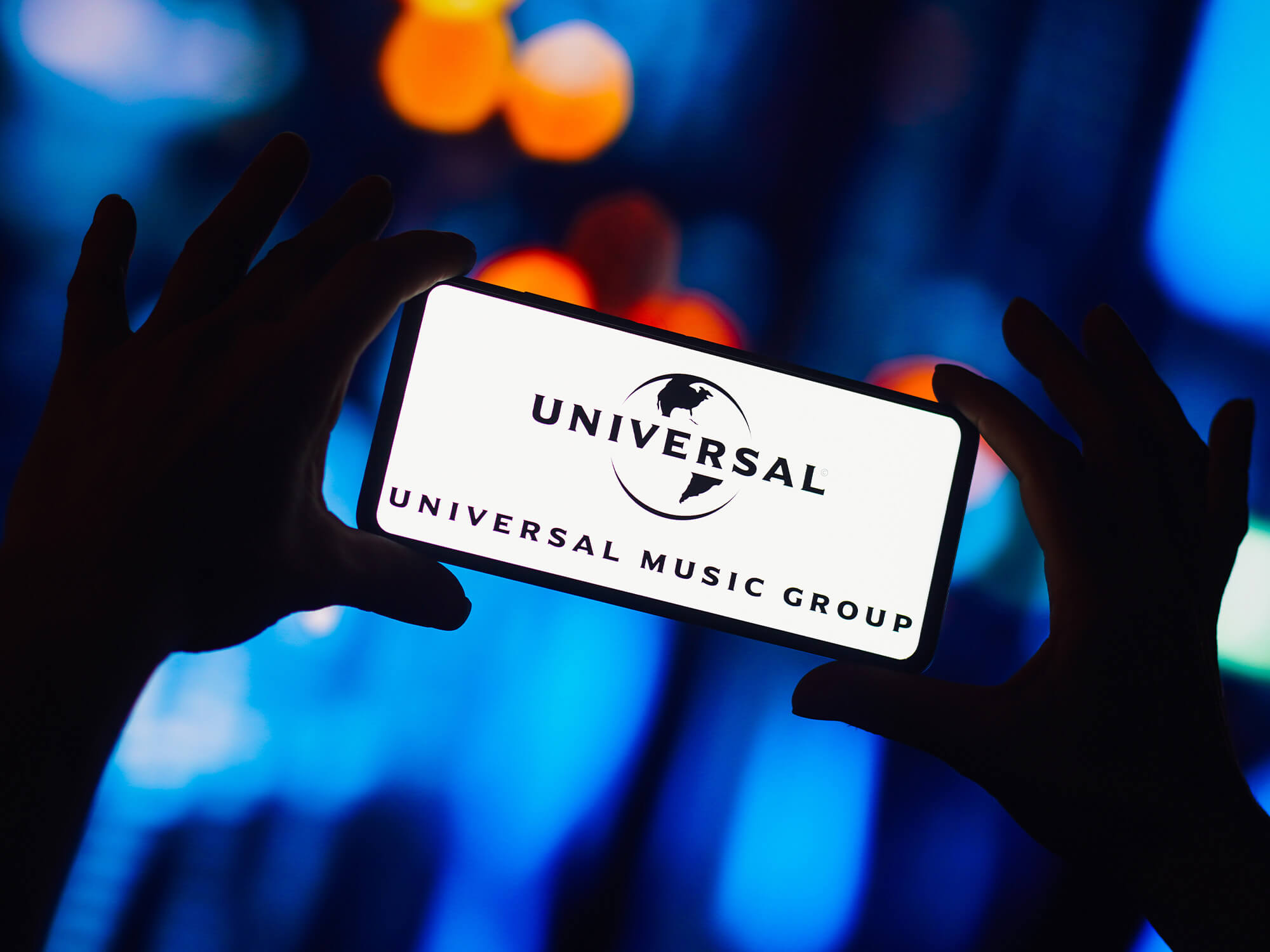 The Universal Music Group logo on a phone screen which is being held up by two hands.