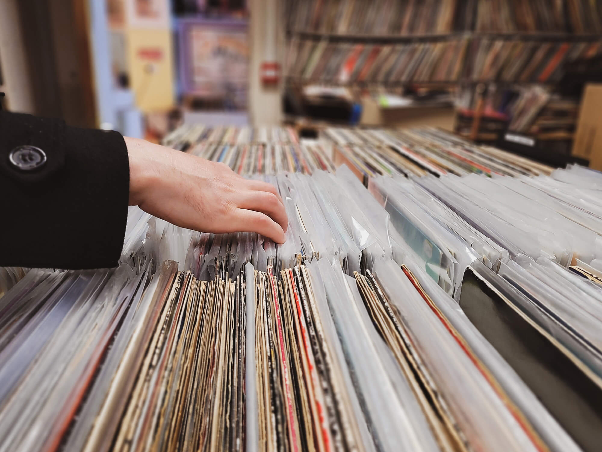 A person's hand flicking through a large collection of vinyl records.