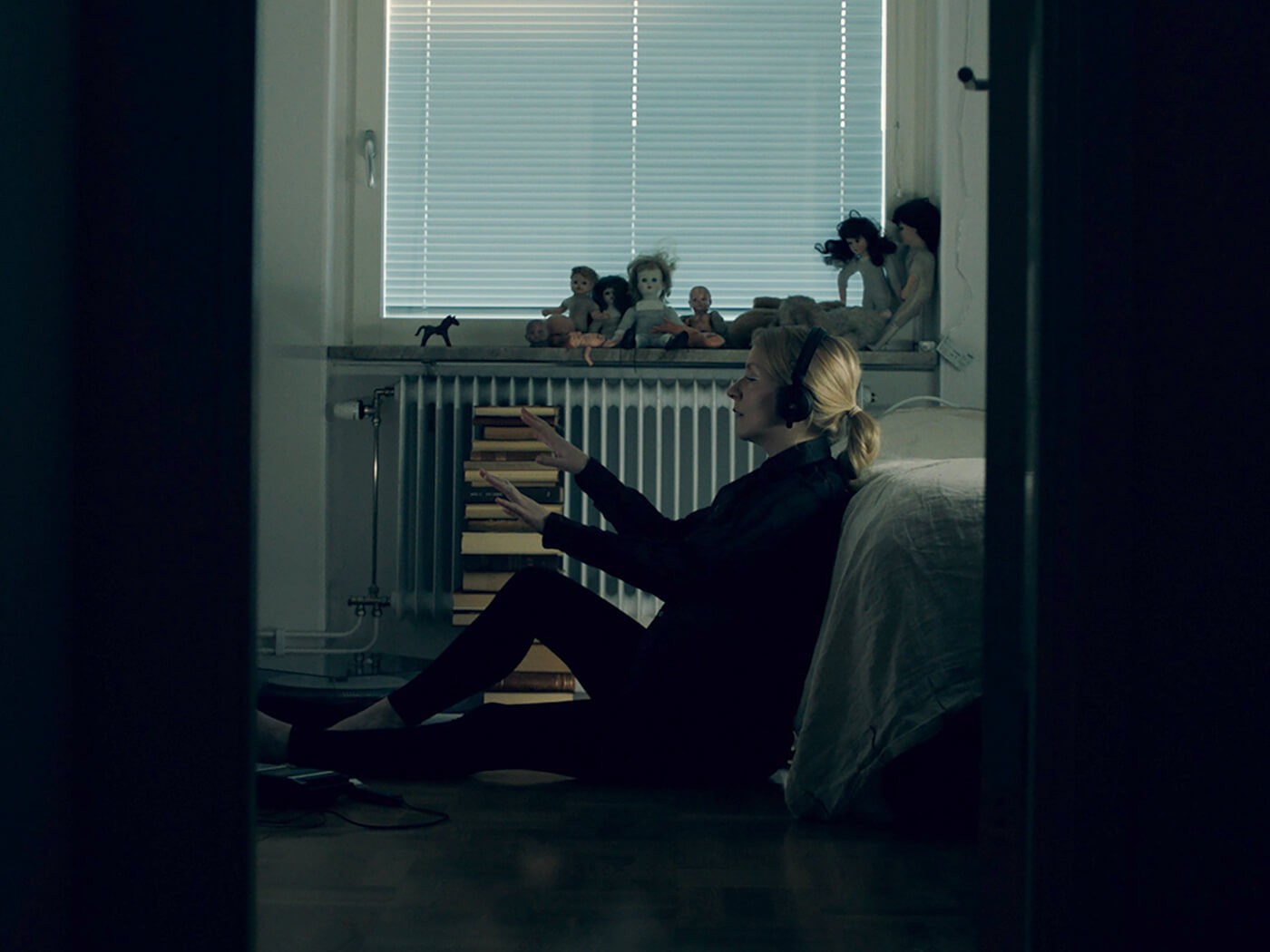 Framed shot of Jonna Lee, the artist behind iamamiwhoami, in a bedroom with headphones on and hands up