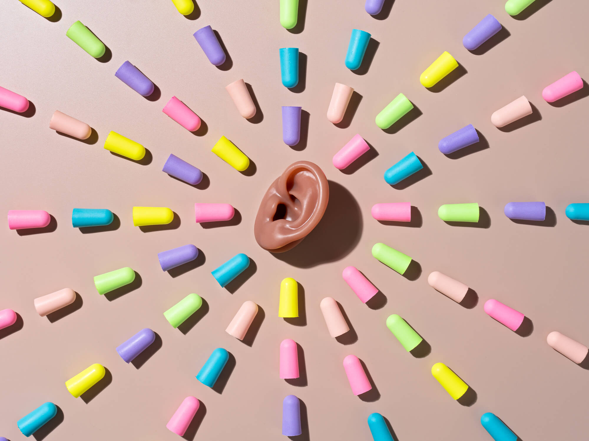 A fake plastic ear surrounded by multi-coloured foam earplugs.