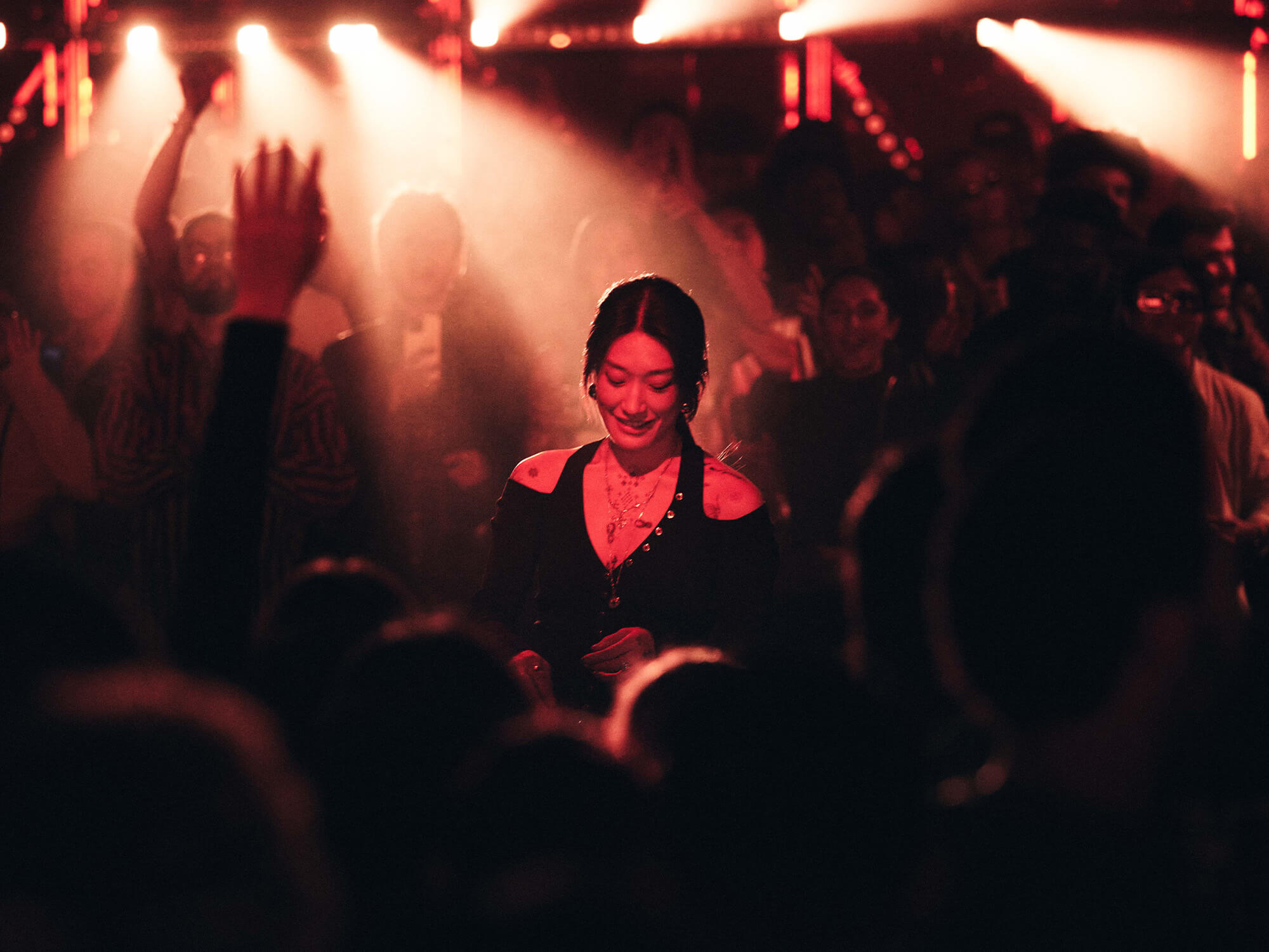 Peggy Gou behind the decks at the event. She is lit up by red lighting and is surrounded by a large crowd who have their arms up in the air.