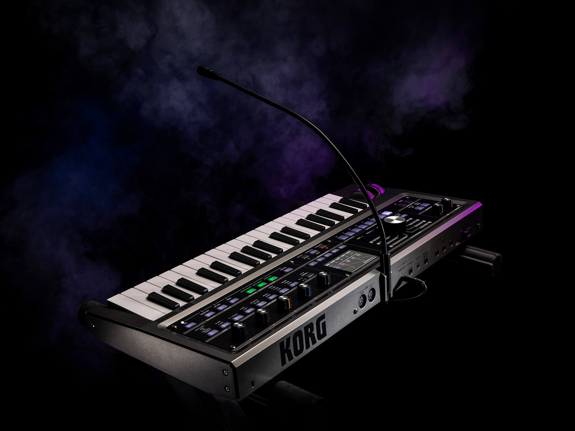 MicroKorg2 on a smokey purple and black background. It is a small synth, with a mini keyboard and a mic which curves over the keys.