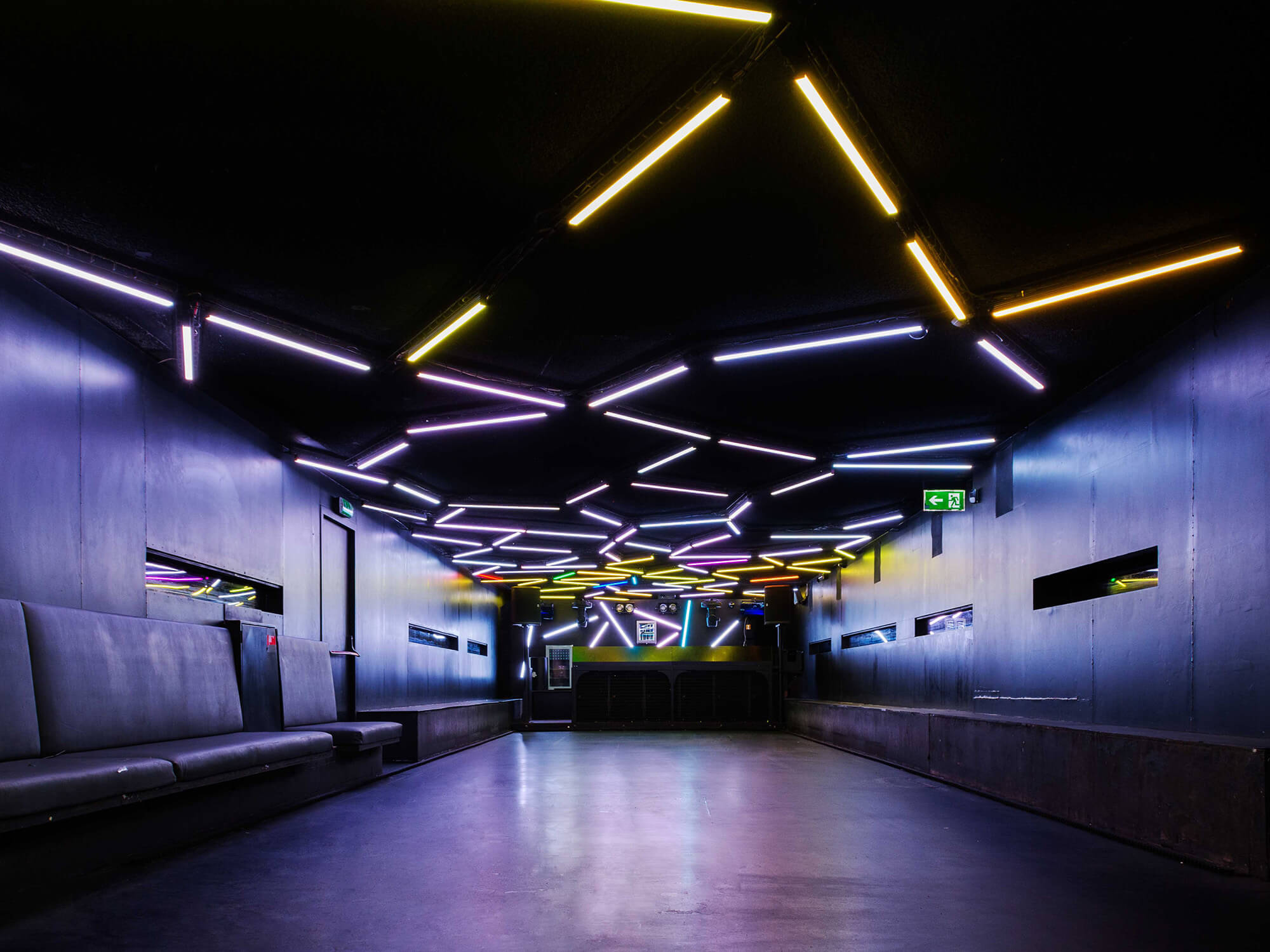 A photo inside of Toffler. The moving booth can be seen at the back of the venue. The walls, floor and ceiling are black. Strips of LED lights decorate the ceiling.