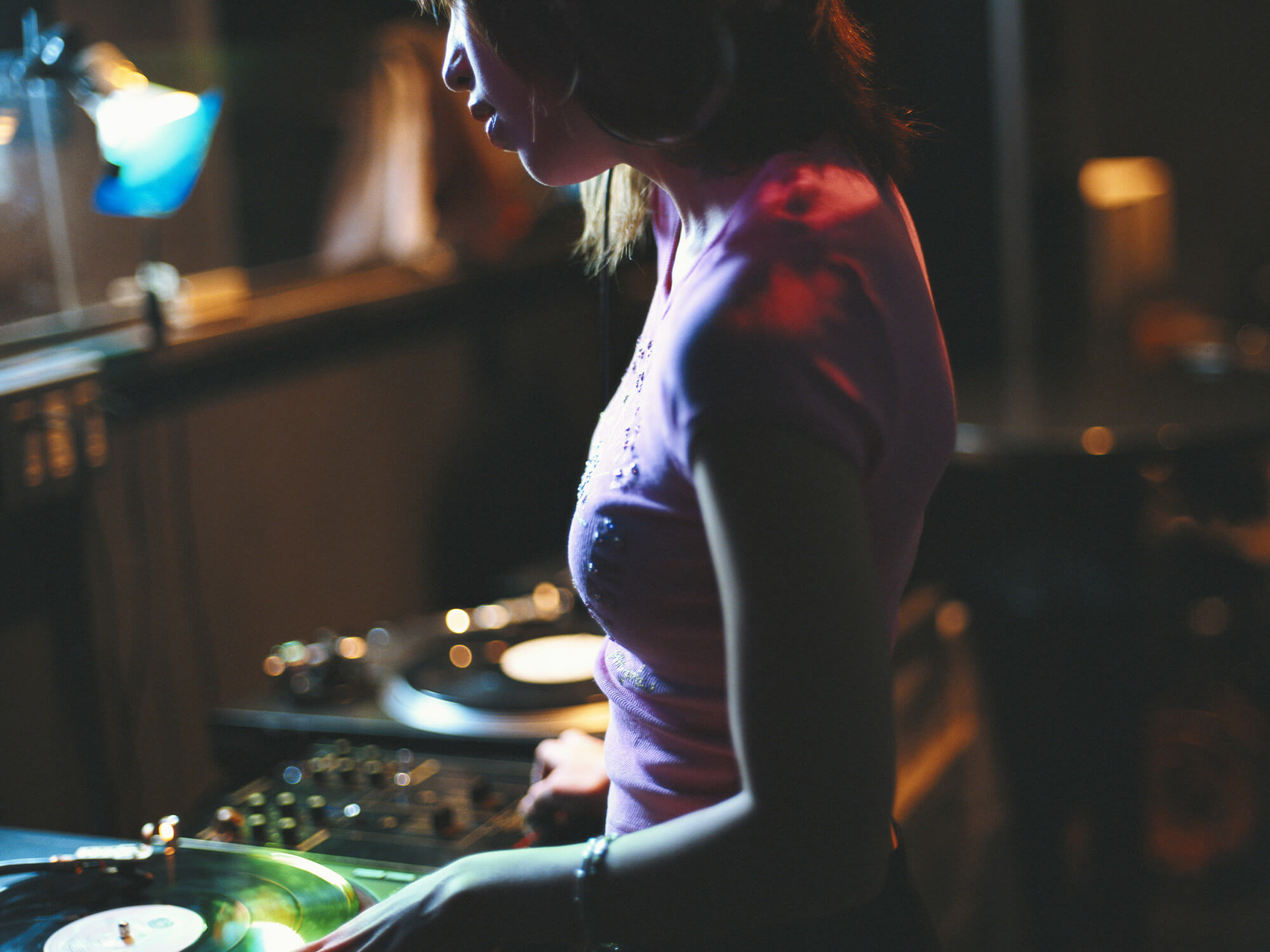 Side profile of a young woman behind DJ decks wearing headphones
