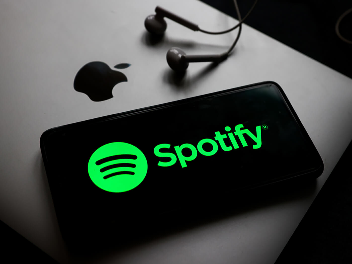 Spotify logo on a phone, alongside a Macbook and a pair of earphones, photo by Beata Zawrzel/NurPhoto via Getty Images