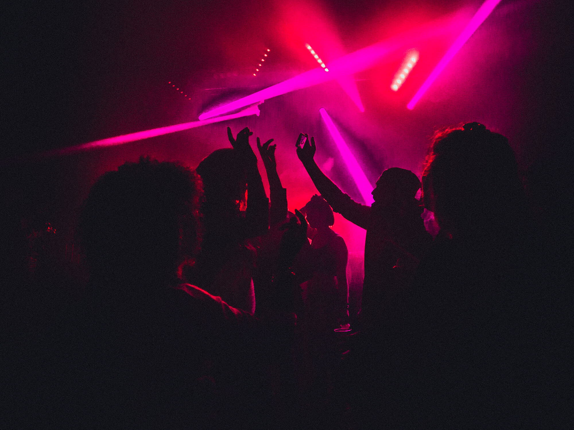 eople dancing in a nightclub with smoke machines and strobe lighting around them.