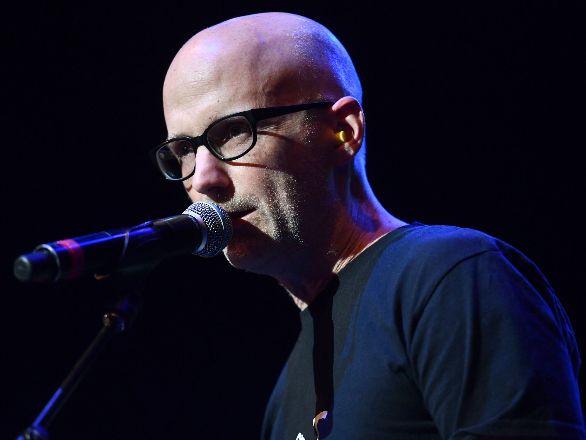 A close up photo of Moby singing into a mic on stage.