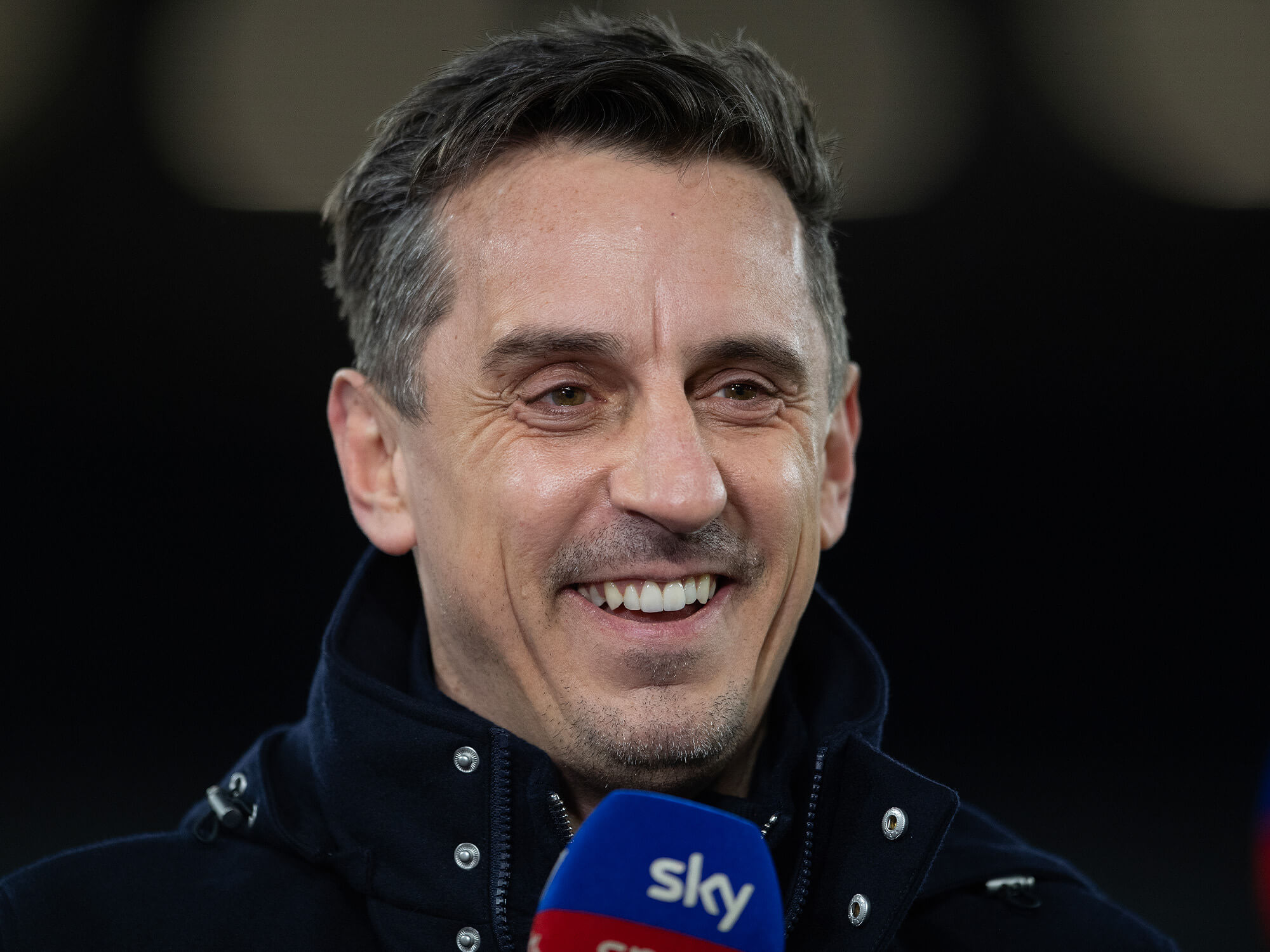 Gary Neville holding a football pundit mic and smiling