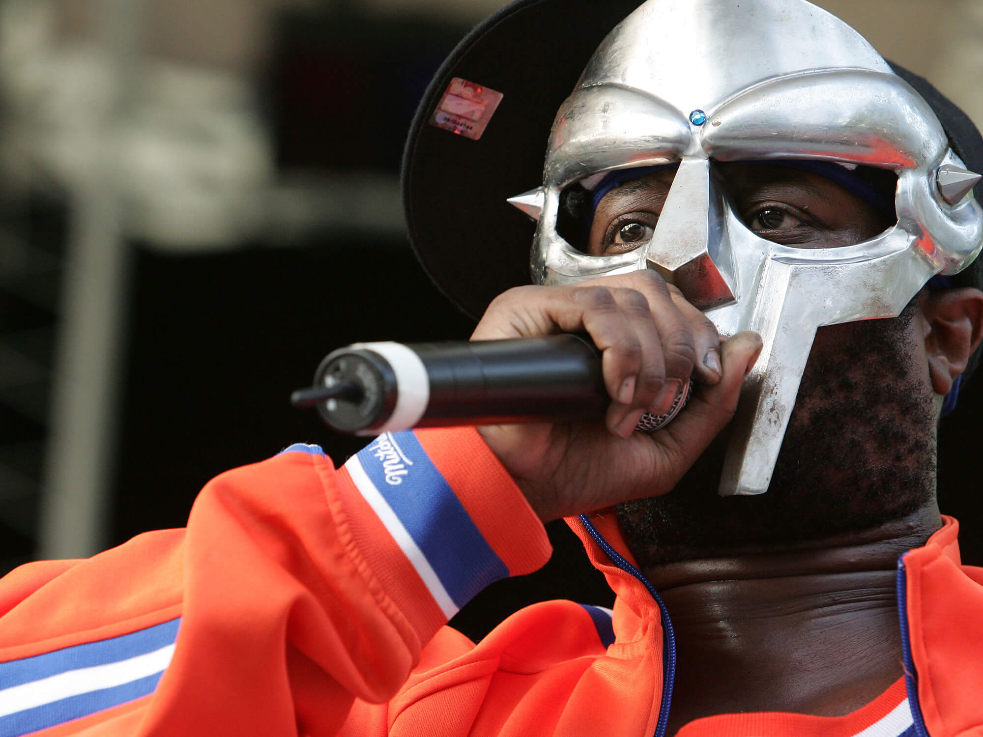 MF DOOM in his signature metal mask. He is on stage and is holding a mic.